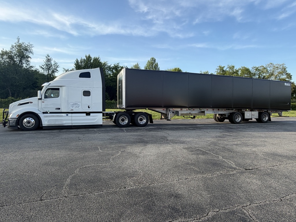 A CARVI Logistics tractor coupled to a flatbed trailer with a black rolling tarp over the load.