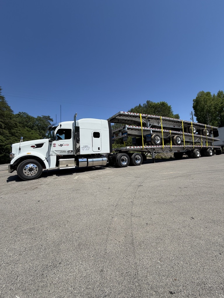 A CARVI Logistics tractor hauling an open-deck trailer load on a clear day.